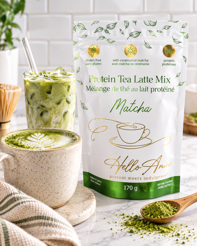 A stand-up pouch of HelloAmino Protein Tea Latte Mix Matcha, styled on a marble surface with a prepared matcha latte, a wooden spoon of green powder, and a mug in a bright kitchen setting.